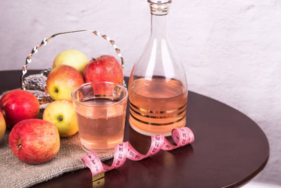 Bottle and glass of apple cider vinegar for weight loss with fresh apples and measuring tape on table