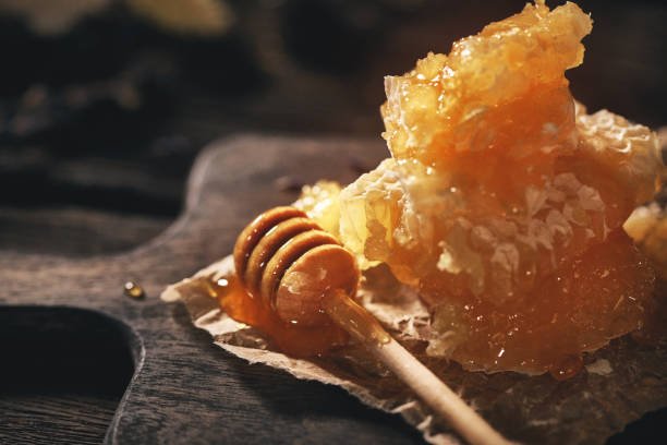 Close up of golden honeycomb and honey dipper on rustic wooden board illustrating how is honeydew honey made naturally