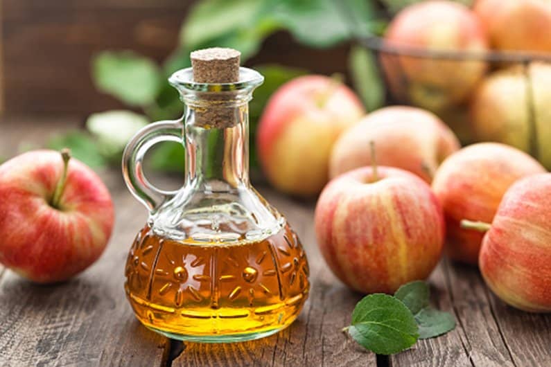 Glass cruet of apple cider vinegar surrounded by fresh apples on wooden table for natural remedies with apple cider vinegar