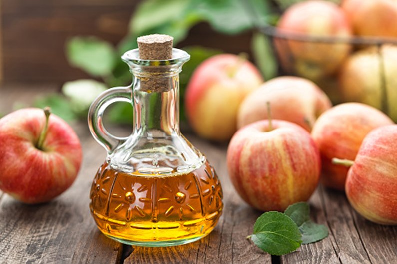 Glass cruet of apple cider vinegar surrounded by fresh apples on wooden table for natural remedies with apple cider vinegar