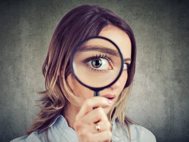 KFactor Manuka Honey explained by a woman holding a magnifying glass up to her eye in close up inspection