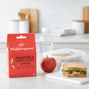 Wedderspoon Manuka Honey Drops Ginger packaging on a kitchen counter with an apple and sandwich.