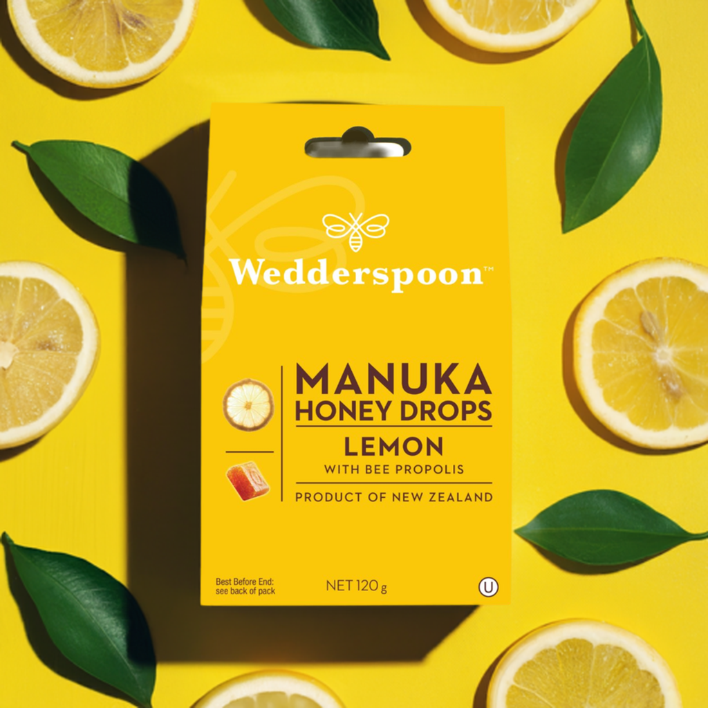 Wedderspoon Manuka Honey Drops Lemon package on a yellow background with lemon slices and leaves.