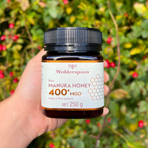 Wedderspoon Raw Manuka Honey 400 MGO 250g Unpasteurised jar held in hand with natural green background
