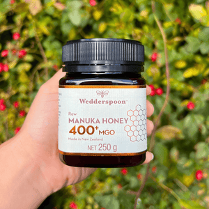Wedderspoon Raw Manuka Honey 400 MGO 250g Unpasteurised jar held in hand with natural green background