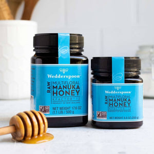 Wedderspoon Raw Manuka honey KFactor 12 500g jar with smaller jar and honey dipper on white surface