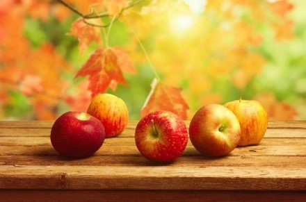 Fresh apples on a wooden table with autumn leaves and sunlight for autumn recipes with manuka honey