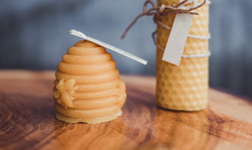 Two beeswax candles on a wooden board beehive and rolled honeycomb style illustrating benefits of beeswax candles