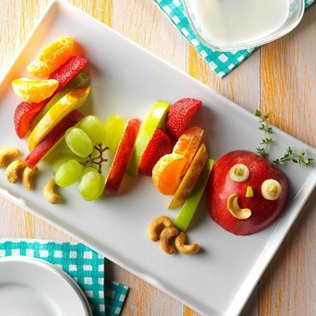 Plate of fruit caterpillar made from apple strawberries grapes orange and cashew pieces as healthy snacks for kids