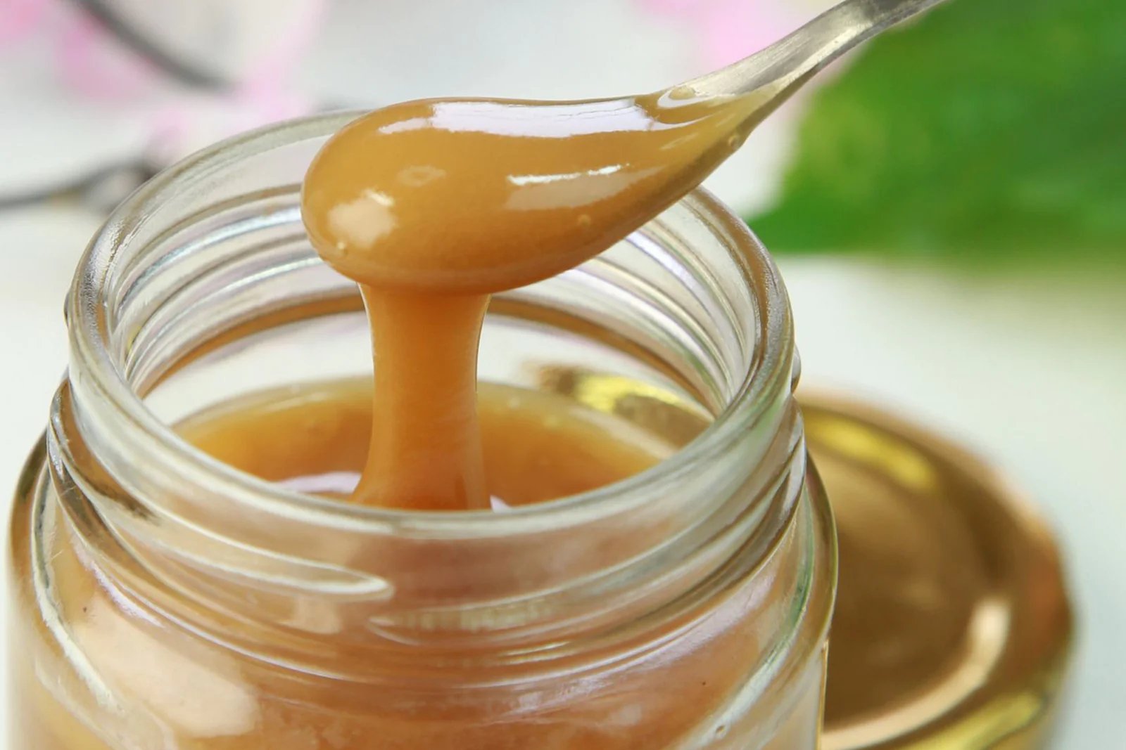 Close up of spoon pouring thick golden Manuka honey into glass jar KFactor vs MGO Manuka honey comparison
