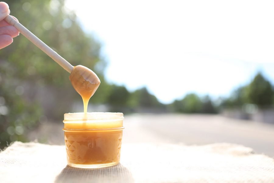 Jar of golden raw honey in sunlight with a wooden dipper dripping honey highlighting raw honey benefits for health