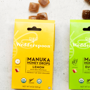 Yellow and green boxes of Wedderspoon Manuka Honey Drops on a light background