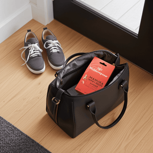 Black handbag with red Ginger Drops on a wooden floor next to Grey Trainers - sports prep.