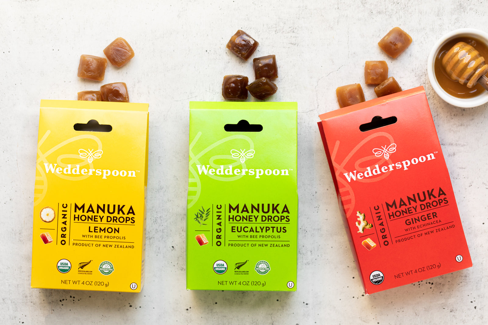 Three Wedderspoon Manuka Honey Drops packages in green, yellow, and red on a white background.