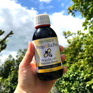 Hand holding Manuka Honey Direct propolis throat syrup with manuka honey bottle outdoors with trees and sky background