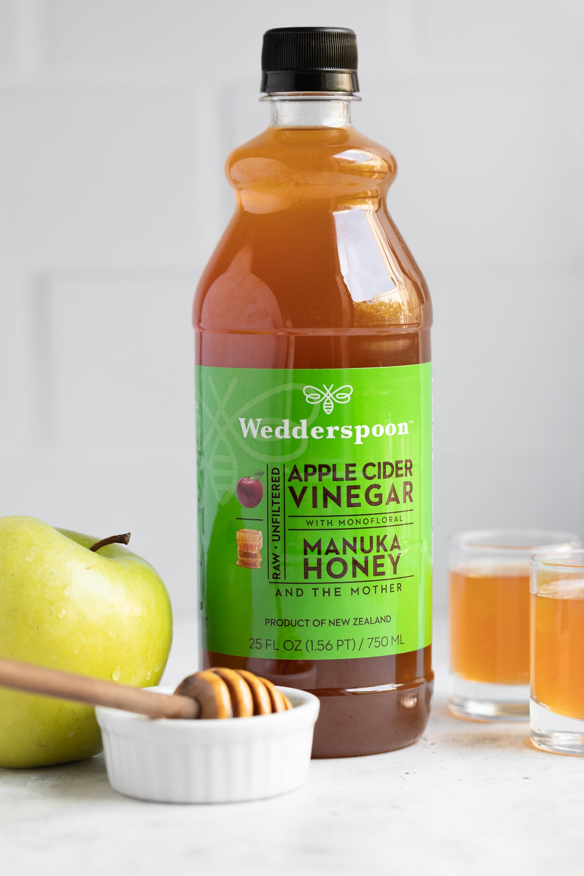 Wedderspoon apple cider vinegar with manuka honey in a 750ml bottle with green label next to apple and honey dipper
