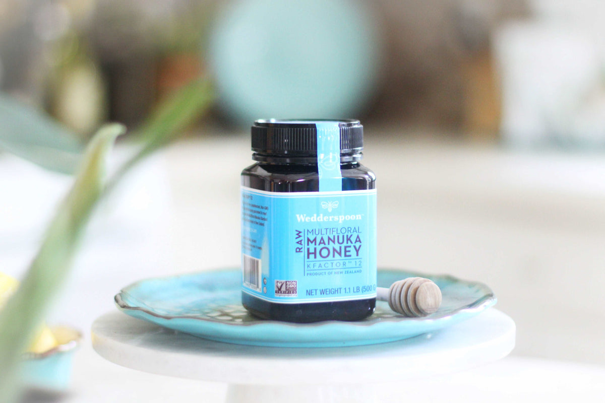 Wedderspoon Raw Manuka honey KFactor 12 jar on blue plate with honey dipper