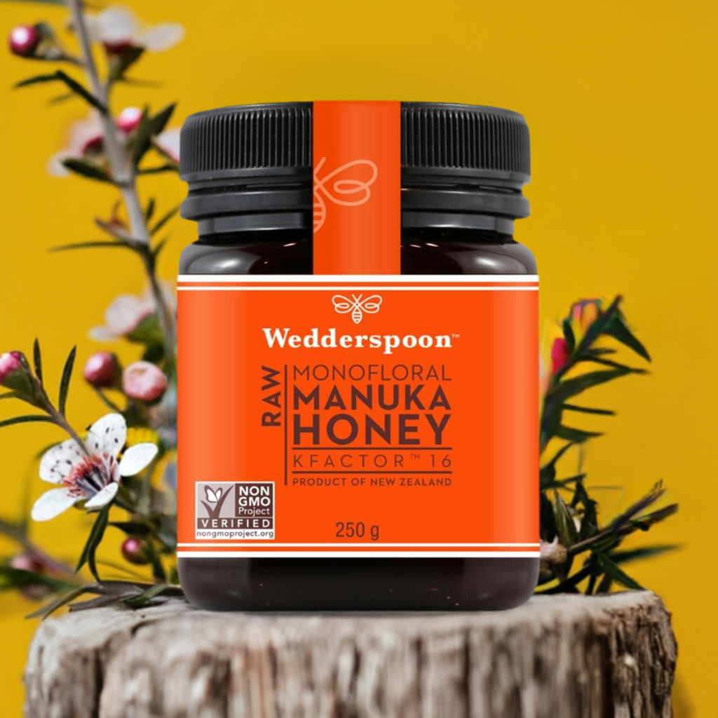 Wedderspoon Raw Manuka Honey 250g jar with orange label on wood log against yellow background