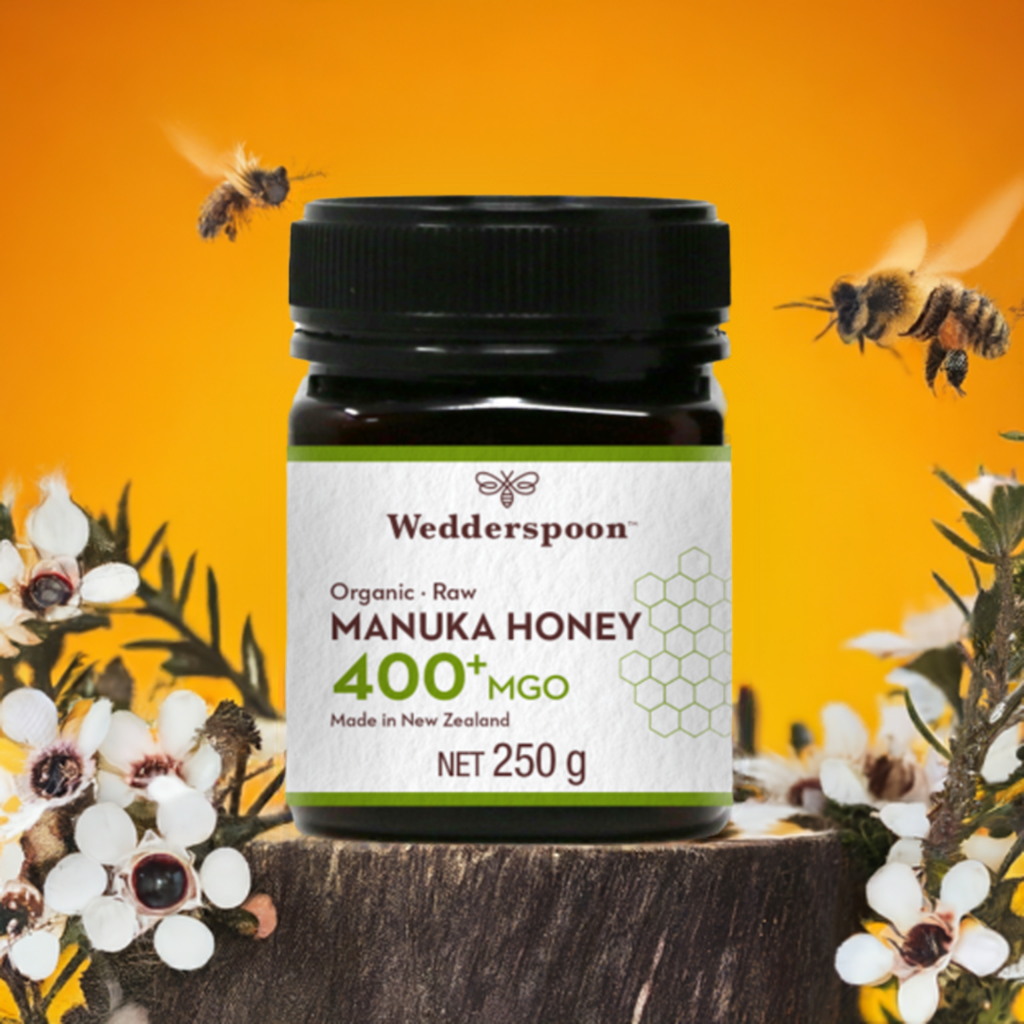 Wedderspoon Organic Raw Manuka Honey 400 MGO 250g jar with honey bees and flowers on wood