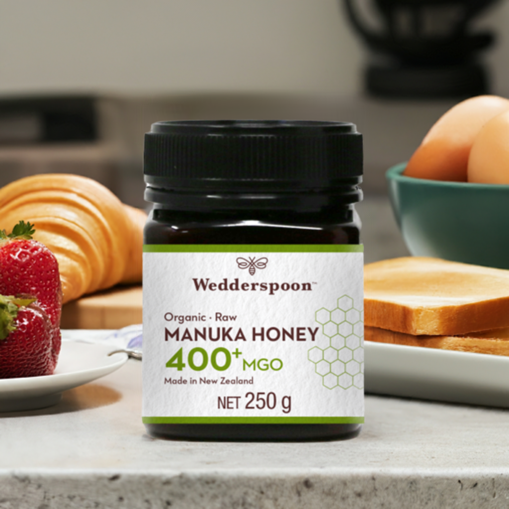 Wedderspoon Organic Raw Manuka Honey 400 MGO 250g jar on kitchen countertop next to breakfast items