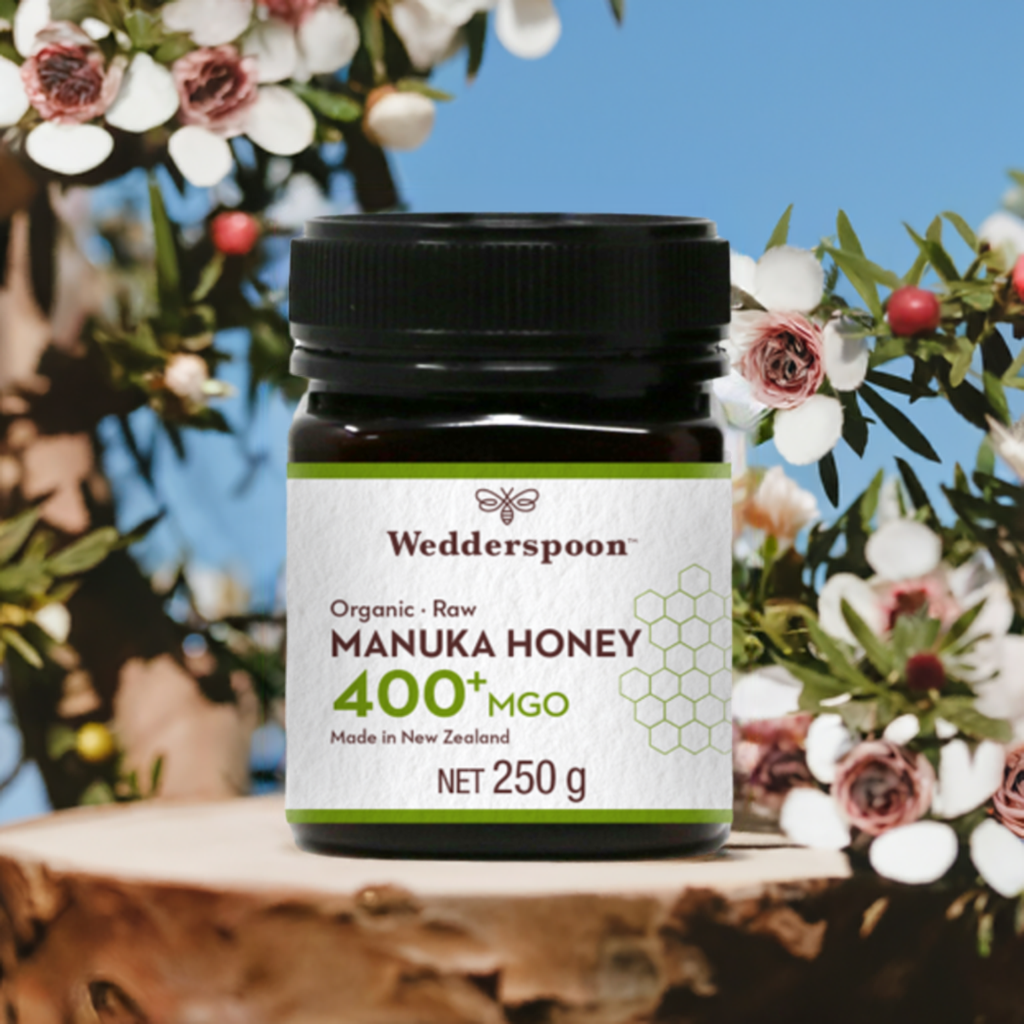 Wedderspoon Organic Raw Manuka Honey 400 MGO 250g jar with floral background and natural wood surface