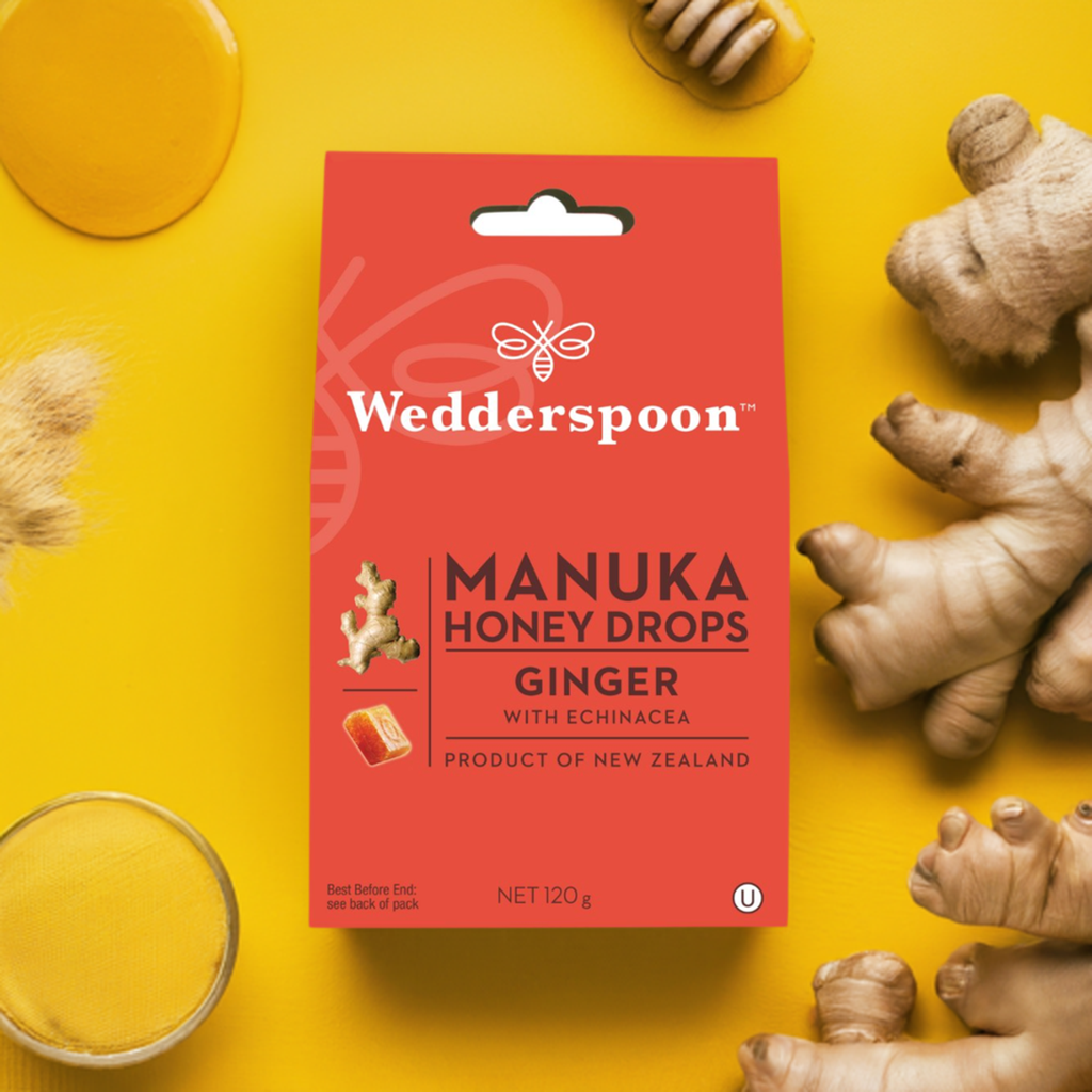 Wedderspoon manuka honey ginger drops throat lozenges with echinacea in red packaging and fresh ginger on yellow background