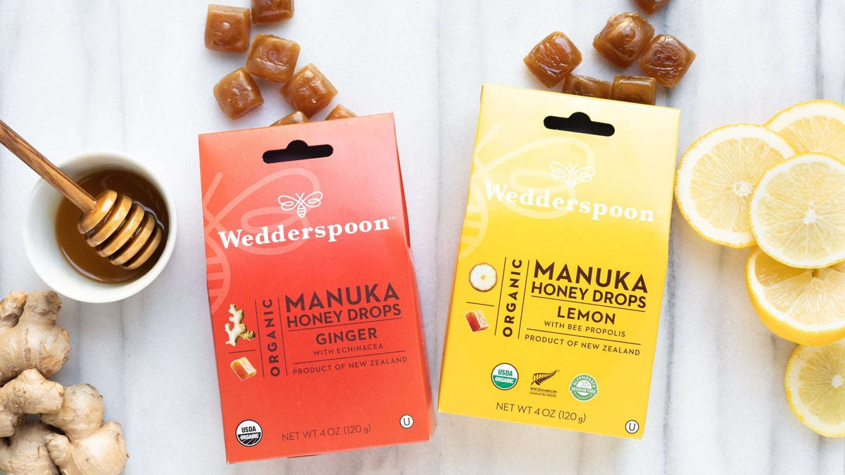 Wedderspoon manuka honey ginger drops and lemon throat lozenges with honey dipper, ginger, and lemon slices