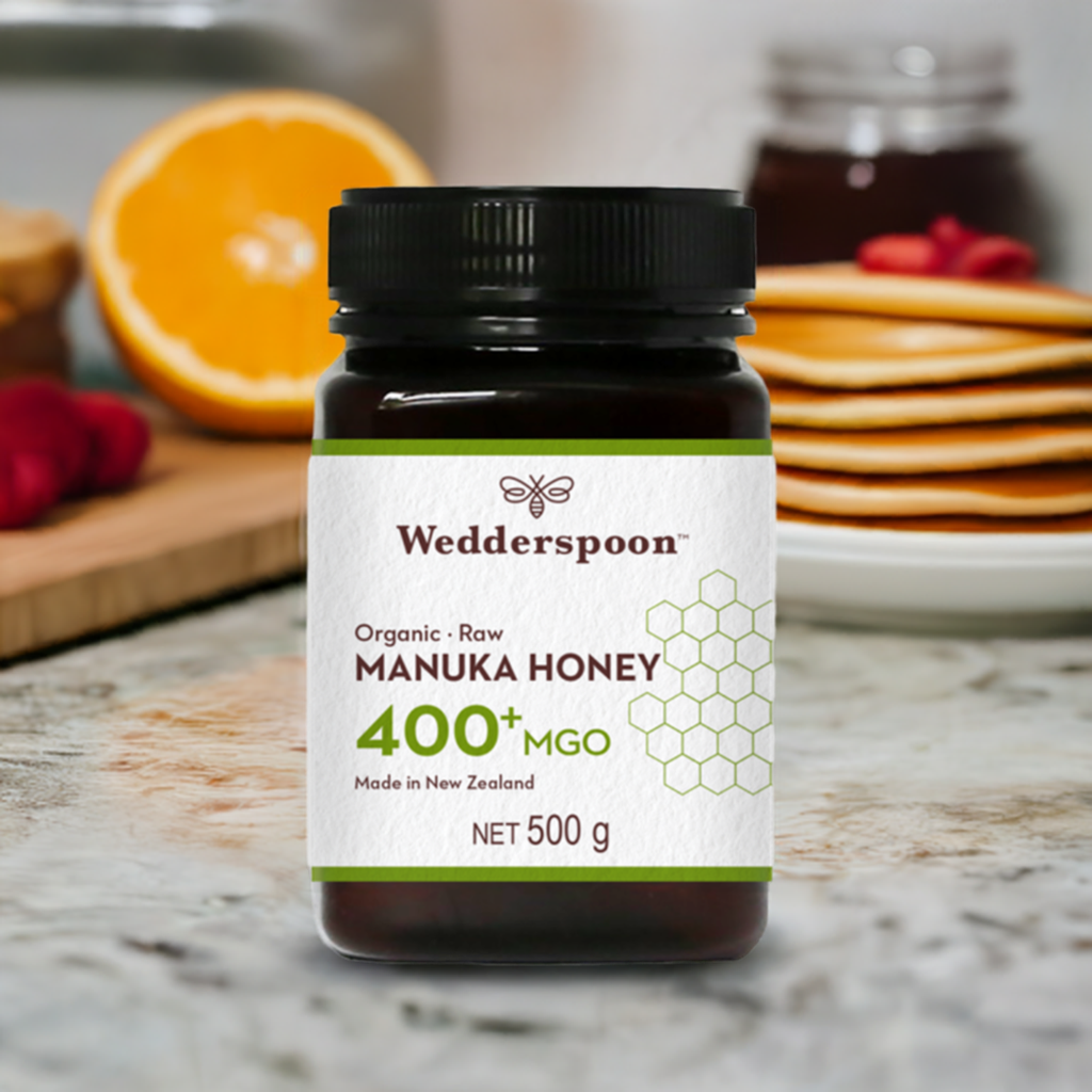Wedderspoon Organic Raw Manuka Honey 400 MGO 500g jar on kitchen counter with breakfast items