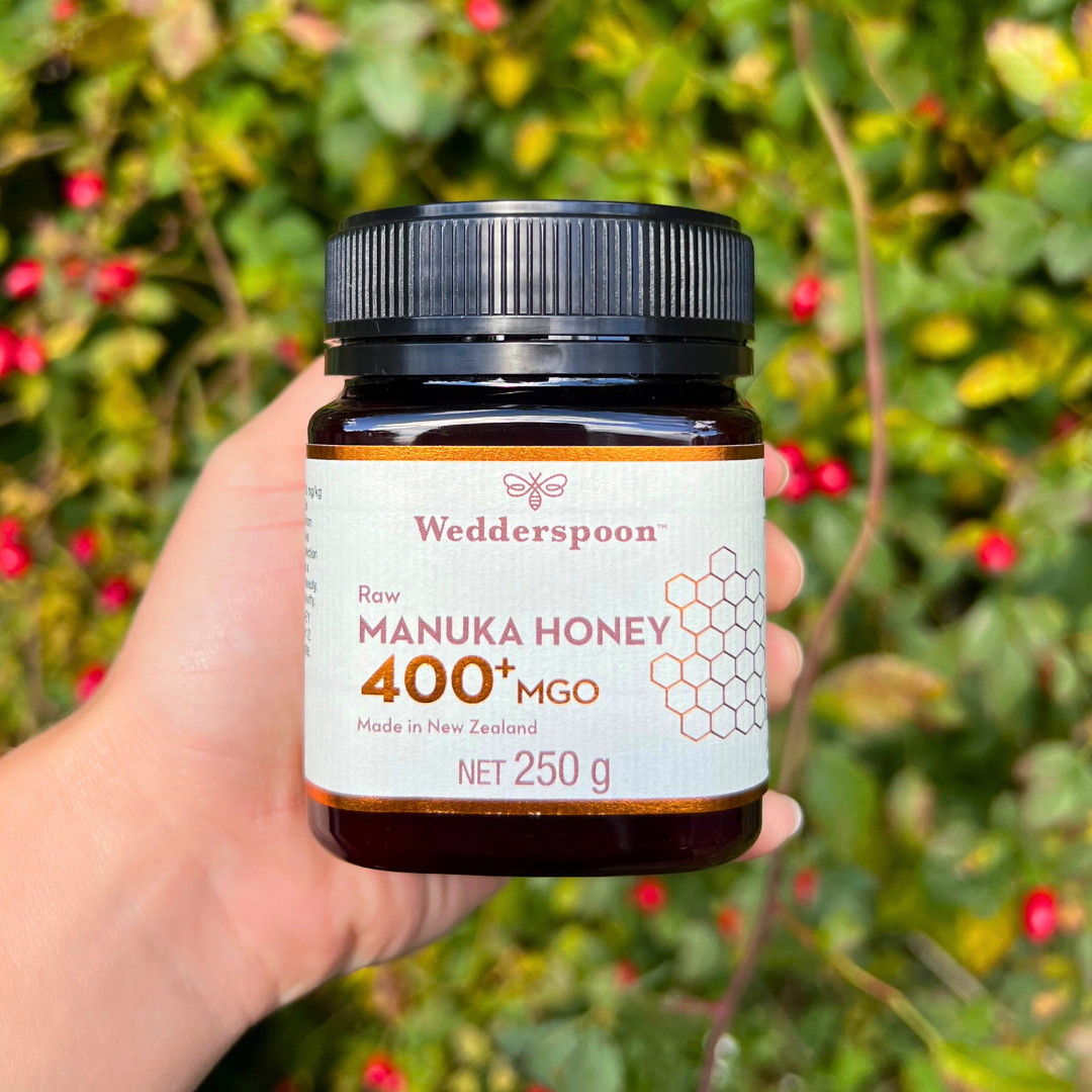 Wedderspoon Raw Manuka Honey 400 MGO 250g Unpasteurised jar held in hand with natural green background