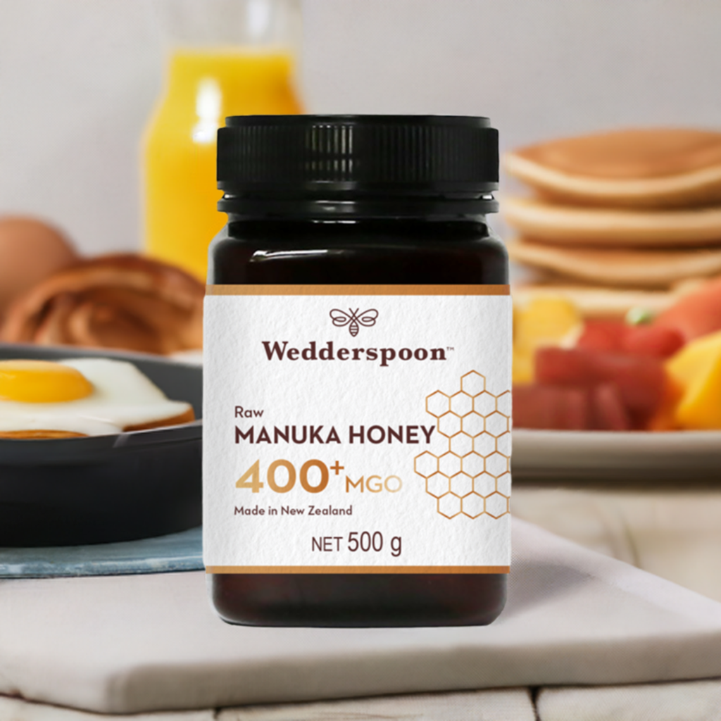 Wedderspoon Raw Manuka Honey 400 MGO 500g jar on table with breakfast items in background