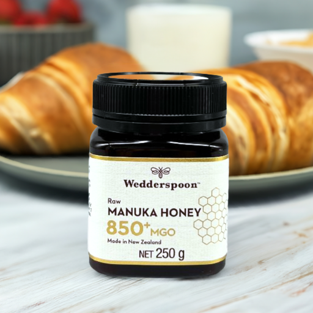 Wedderspoon Raw Manuka Honey 850 MGO 250g . Jar on a breakfast table with croissants and a glass of milk