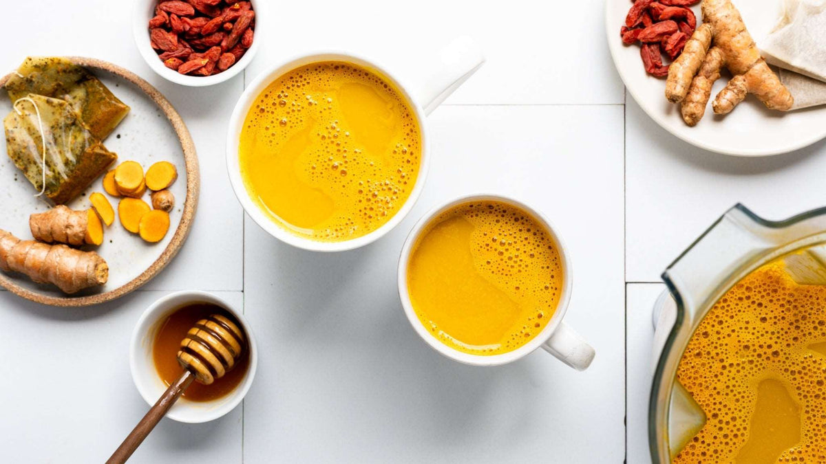 Two cups of turmeric tea with honey and fresh turmeric roots featuring Wedderspoon Raw Manuka honey KFactor 12 500g