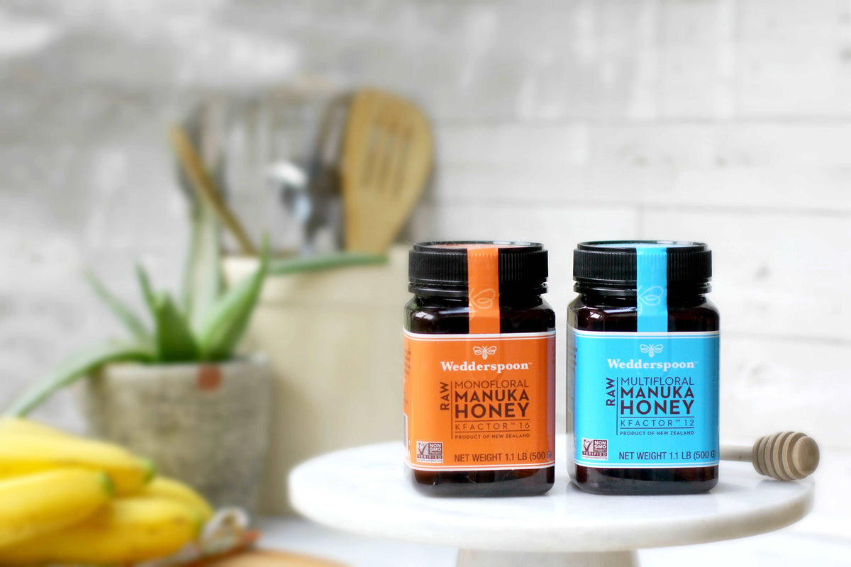 Wedderspoon Raw Manuka Honey KFactor 16 500g Triple Pack jars on kitchen counter with wooden honey dipper
