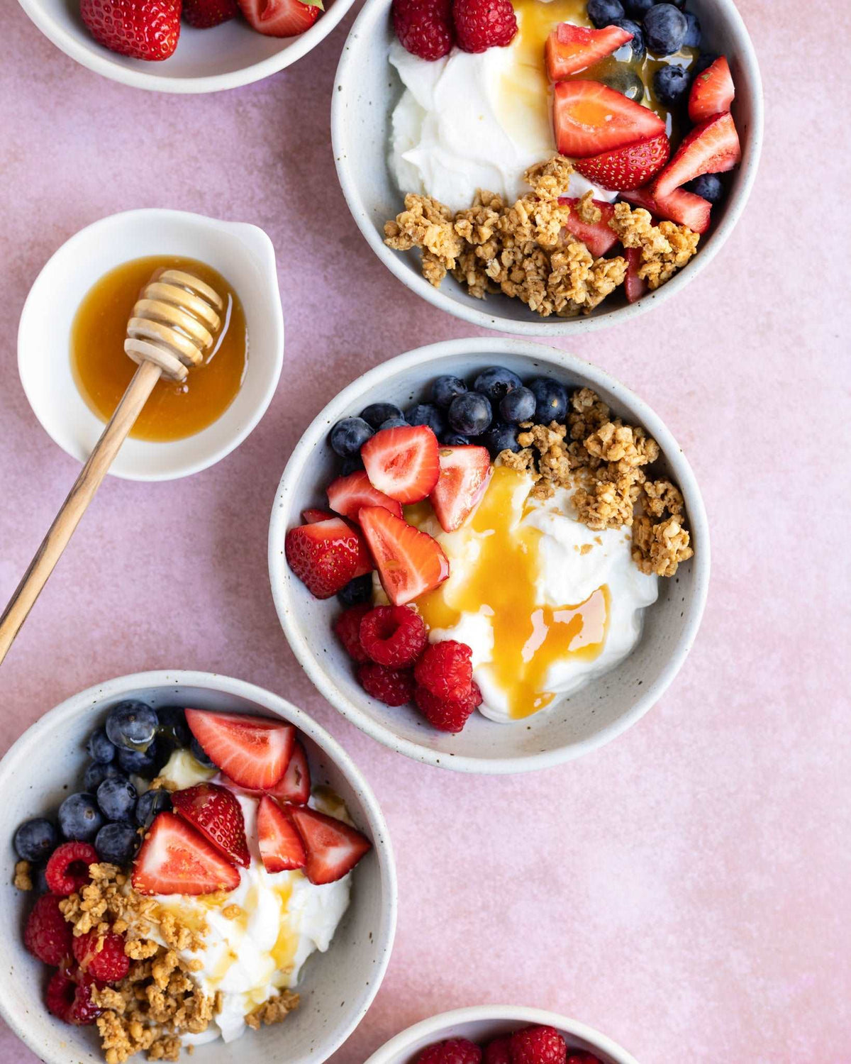 Bowls of yoghurt topped with strawberries, blueberries, raspberries, granola and drizzled with Wedderspoon Raw Manuka Honey KFactor 16 500g Triple Pack