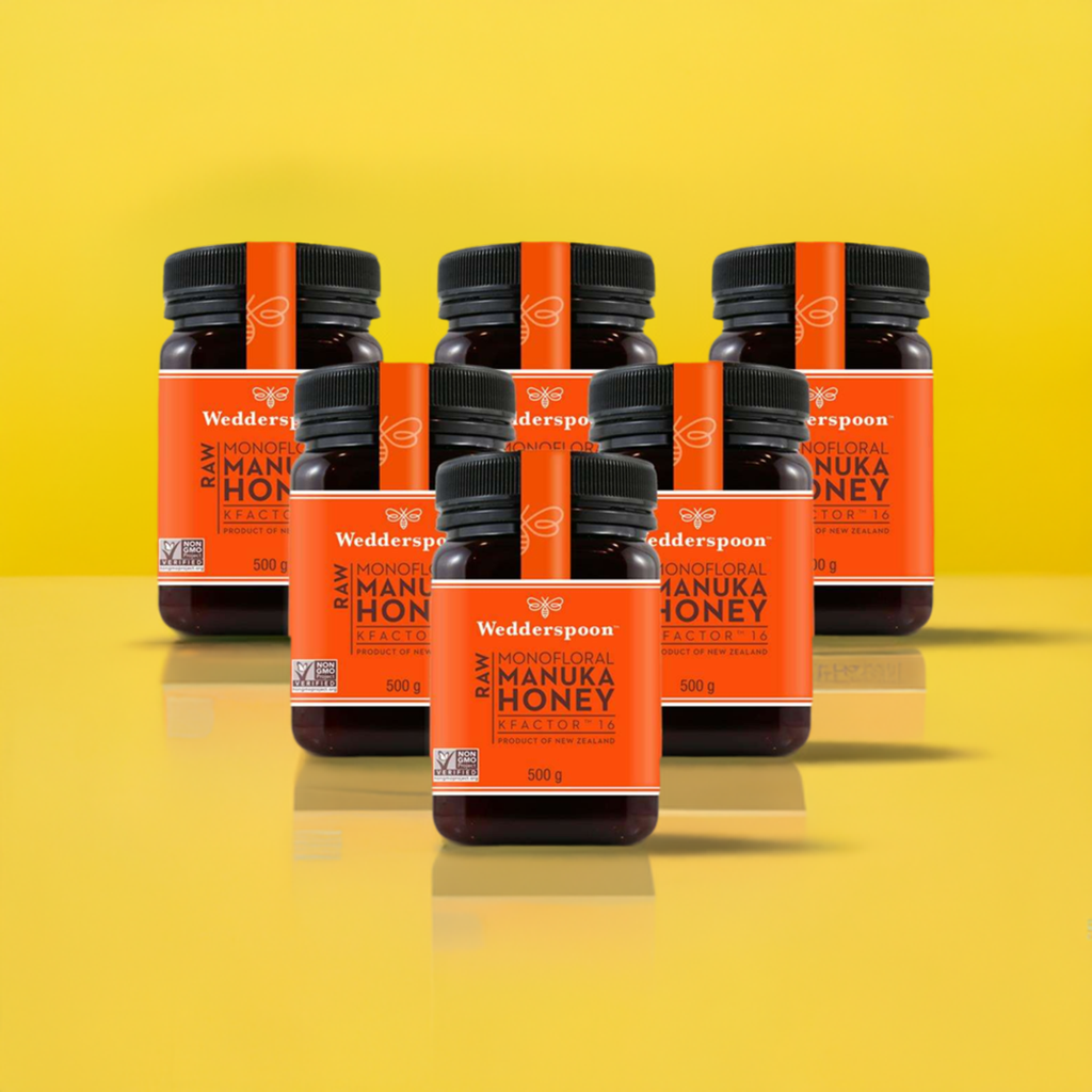 Wedderspoon Raw Manuka Honey KFactor 16 Six Pack jars with orange labels on yellow background